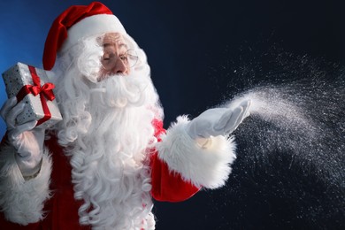 Photo of Santa Claus with Christmas gift blowing snow on dark blue background