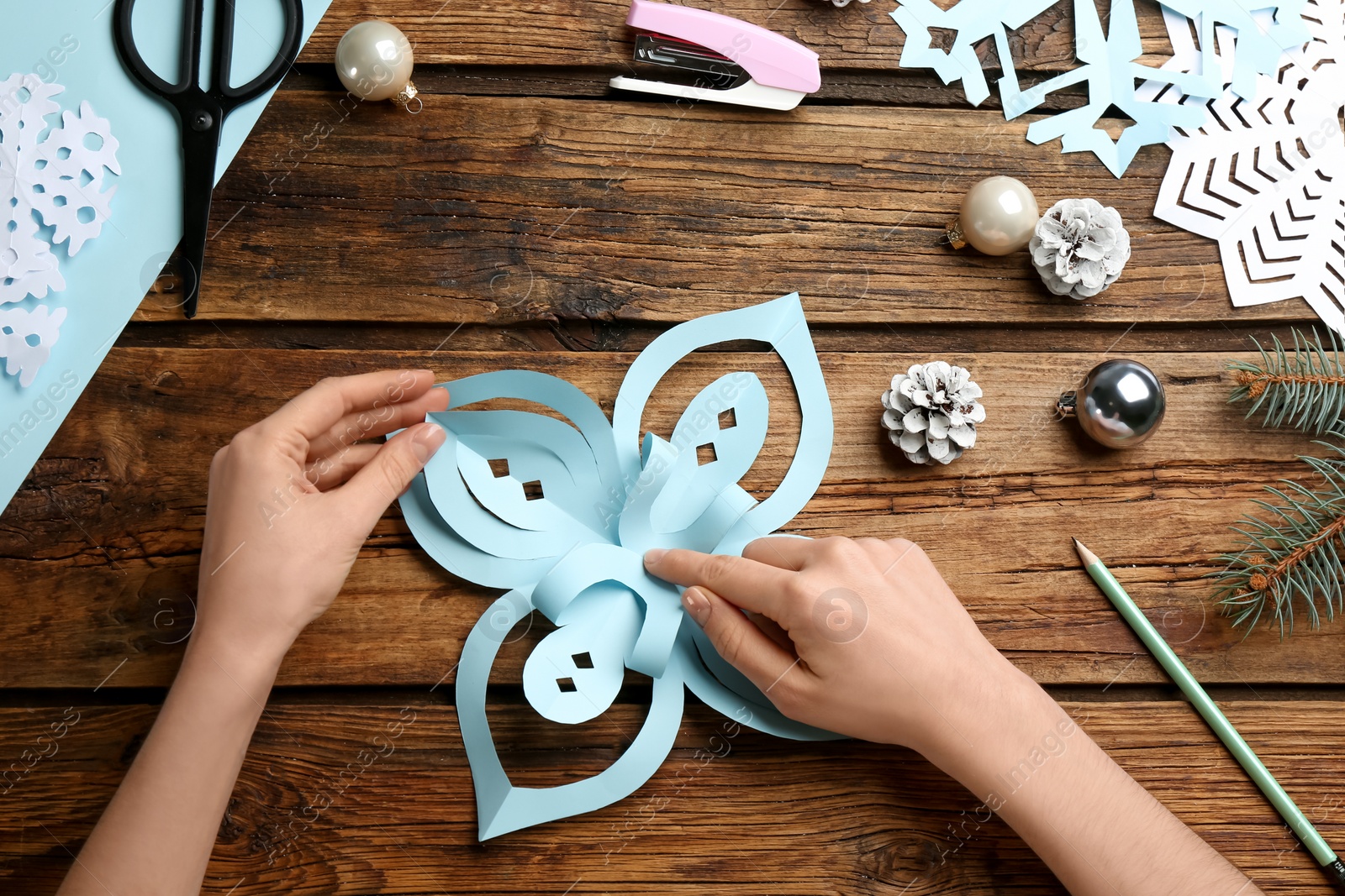 Photo of Woman making paper snowflake at wooden table, top view
