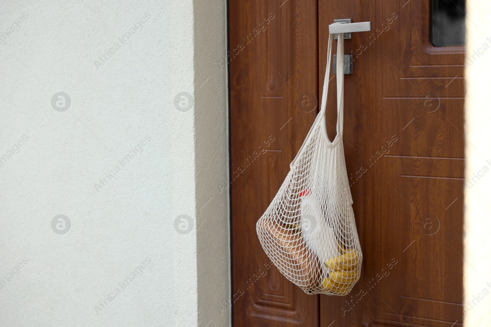 Photo of Helping neighbours. Net bag of products hanging on door outdoors