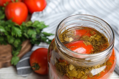 Photo of Pickled tomatoes in glass jar and products on table, closeup view