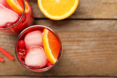 Photo of Tasty cranberry cocktail with ice cubes and orange in glasses on wooden table, flat lay. Space for text