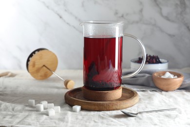 Delicious hibiscus tea in teapot and sugar cubes on table