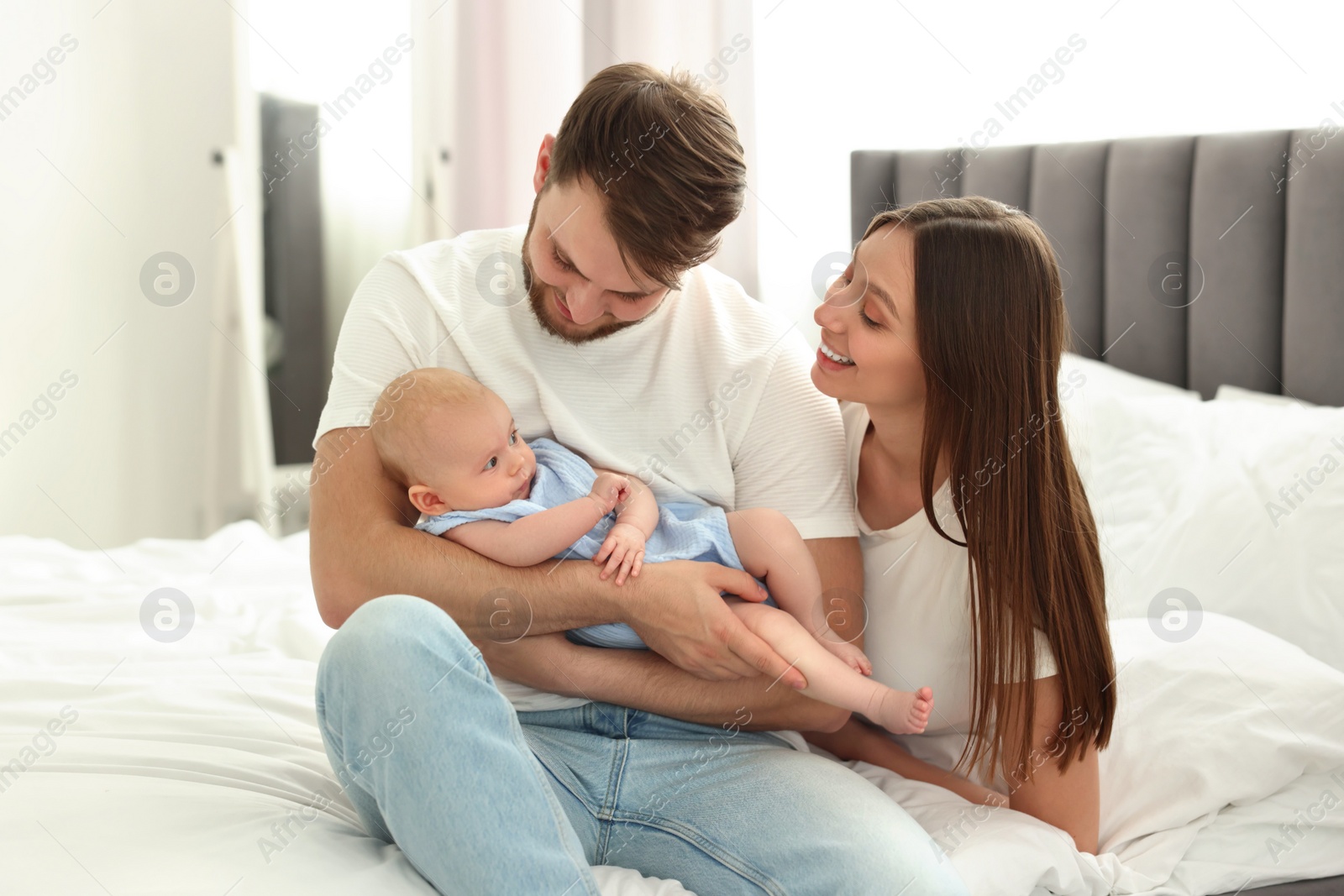 Photo of Happy family. Parents with their cute baby on bed indoors