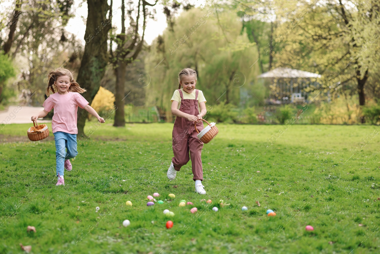 Photo of Easter celebration. Cute little girls hunting eggs outdoors, space for text