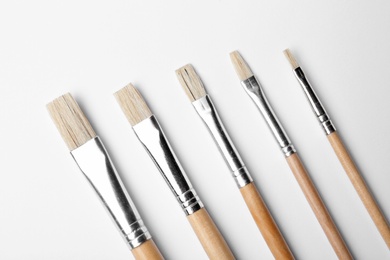 Different paint brushes on white background, top view