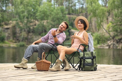Photo of Young couple resting on pier near lake. Camping season