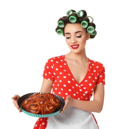 Funny young housewife with hair rollers holding homemade pastry on white background