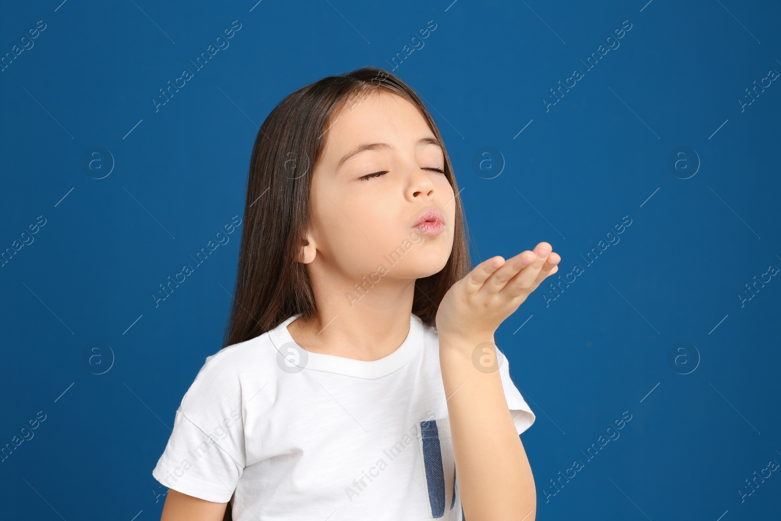 Photo of Cute little girl blowing kiss on blue background