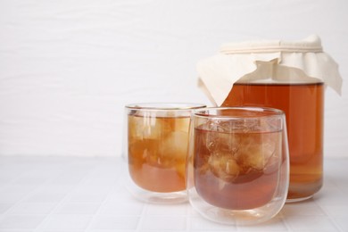 Photo of Tasty kombucha with ice cubes on white tiled table, space for text