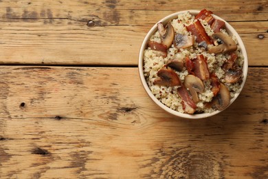 Photo of Tasty quinoa porridge with fried bacon and mushrooms in bowl on wooden table, top view. Space for text