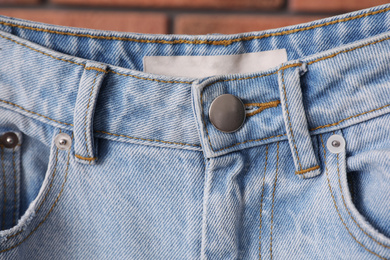 Photo of Modern stylish jeans near brick wall, closeup