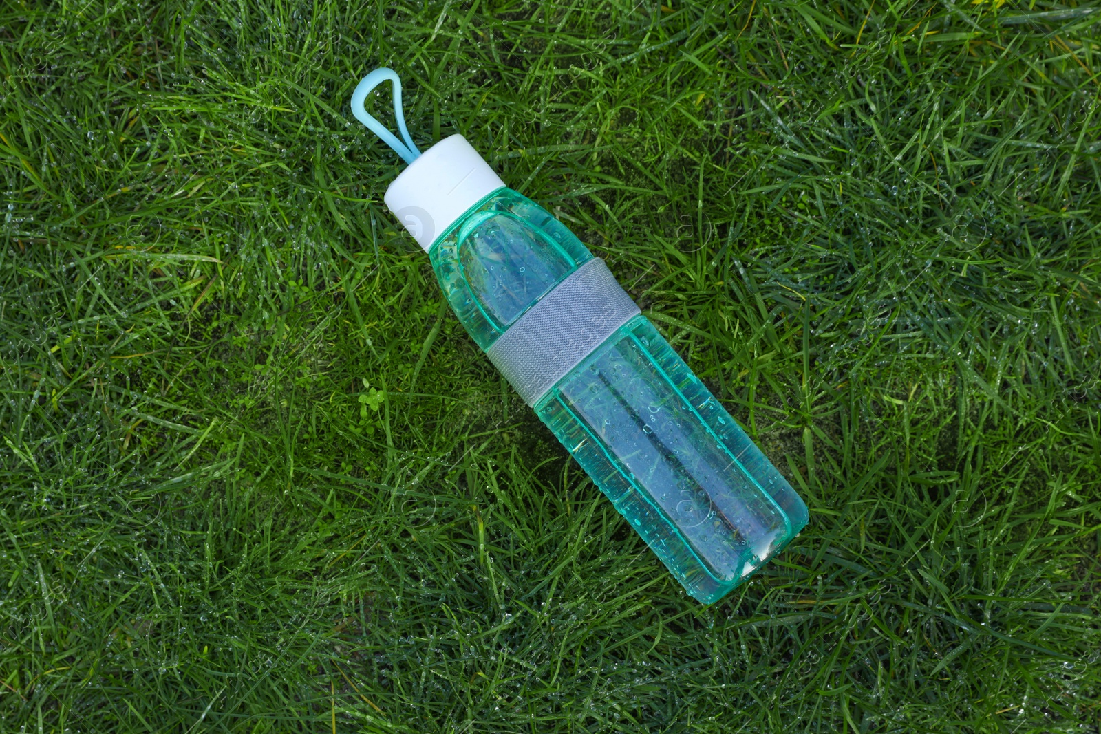 Photo of Glass bottle of fresh water on green grass outdoors, top view