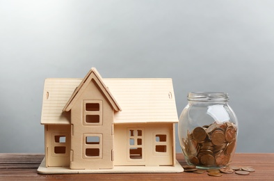 Photo of House model and coins on wooden table against light grey background. Money savings