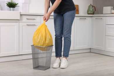 Photo of Woman taking garbage bag out of trash bin in kitchen, closeup