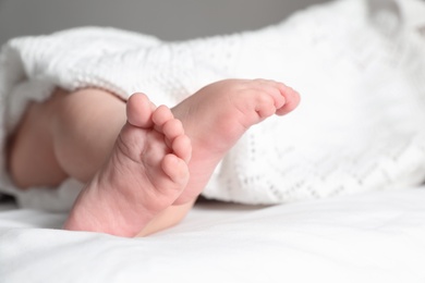 Photo of Little baby with cute feet lying on bed, closeup. Space for text