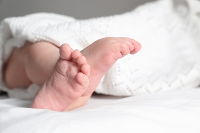 Little baby with cute feet lying on bed, closeup. Space for text