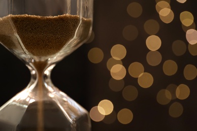 Photo of Hourglass with flowing sand against blurred lights, closeup. Christmas countdown