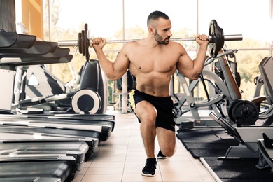 Strong young man lifting barbell in gym