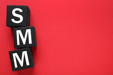 Photo of Black cubes with abbreviation SMM (Social media marketing) on red background, flat lay. Space for text