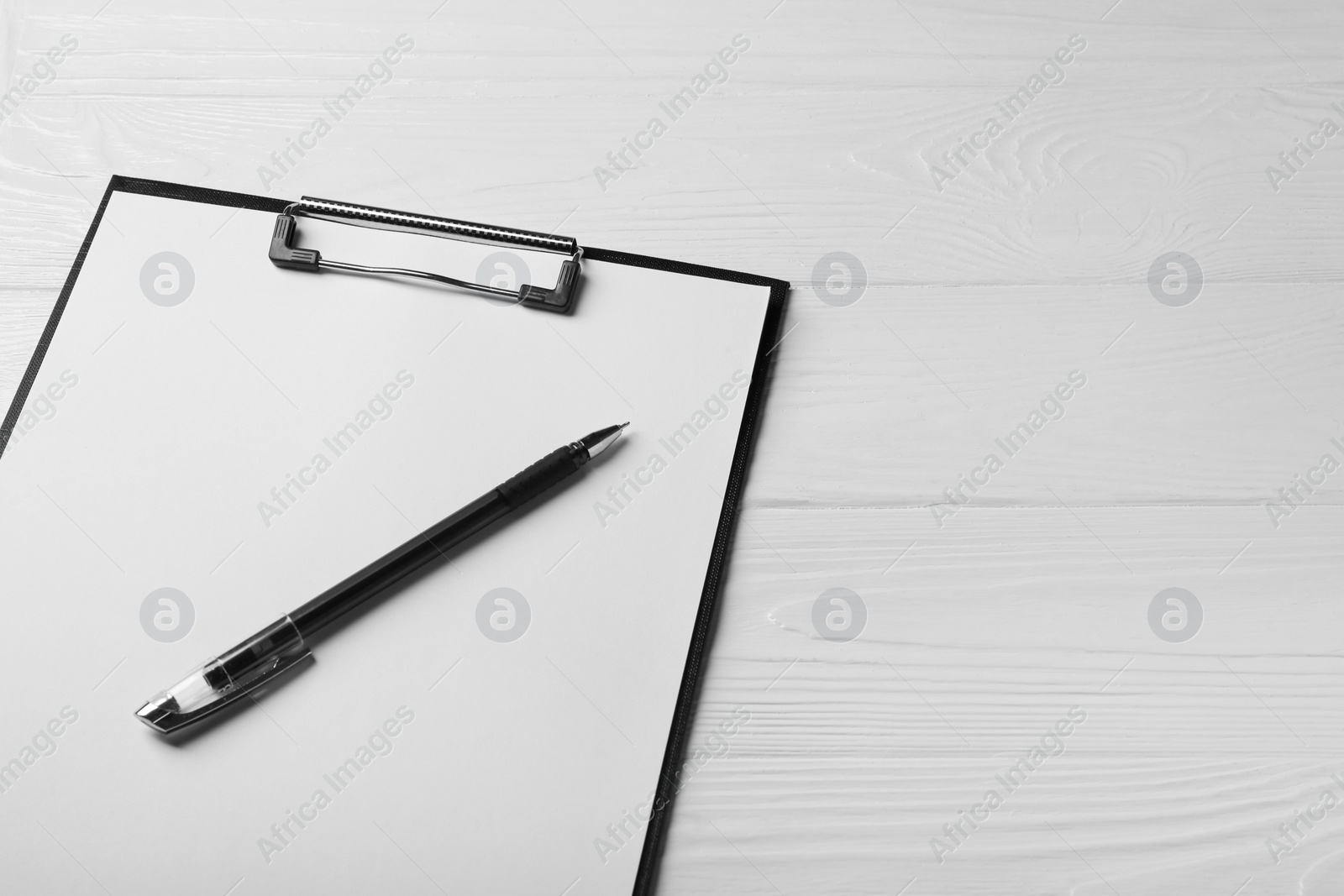 Photo of New clipboard with sheet of blank paper and pen on white wooden table, above view. Space for text