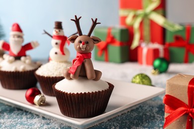 Photo of Different beautiful Christmas cupcakes on blue table with festive decor and snow