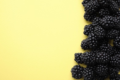 Photo of Tasty ripe blackberries on yellow background, flat lay. Space for text