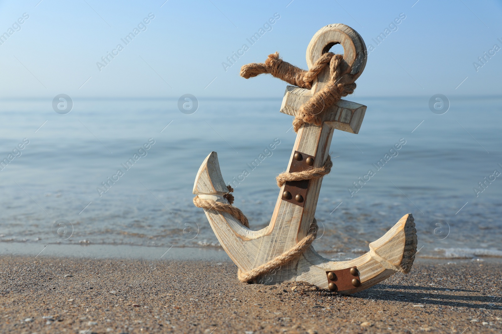 Photo of Wooden anchor with rope on sand near sea. Space for text