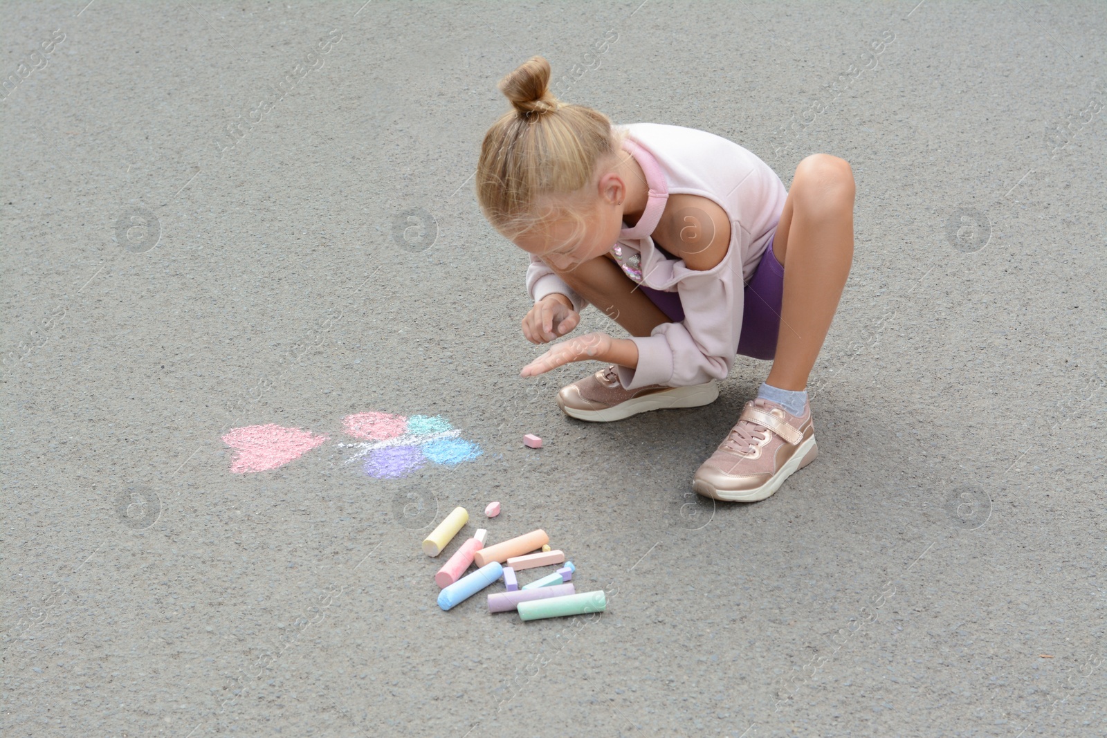 Photo of Little child drawing butterfly and heart with chalk on asphalt