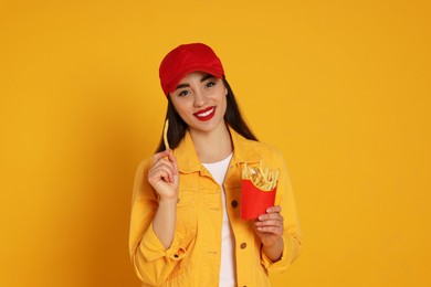 Beautiful young woman with French fries on yellow background