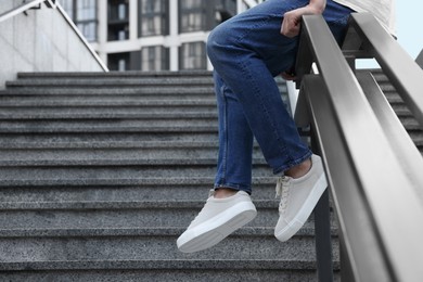 Photo of Man in stylish sneakers sitting on railing outdoors, closeup. Space for text