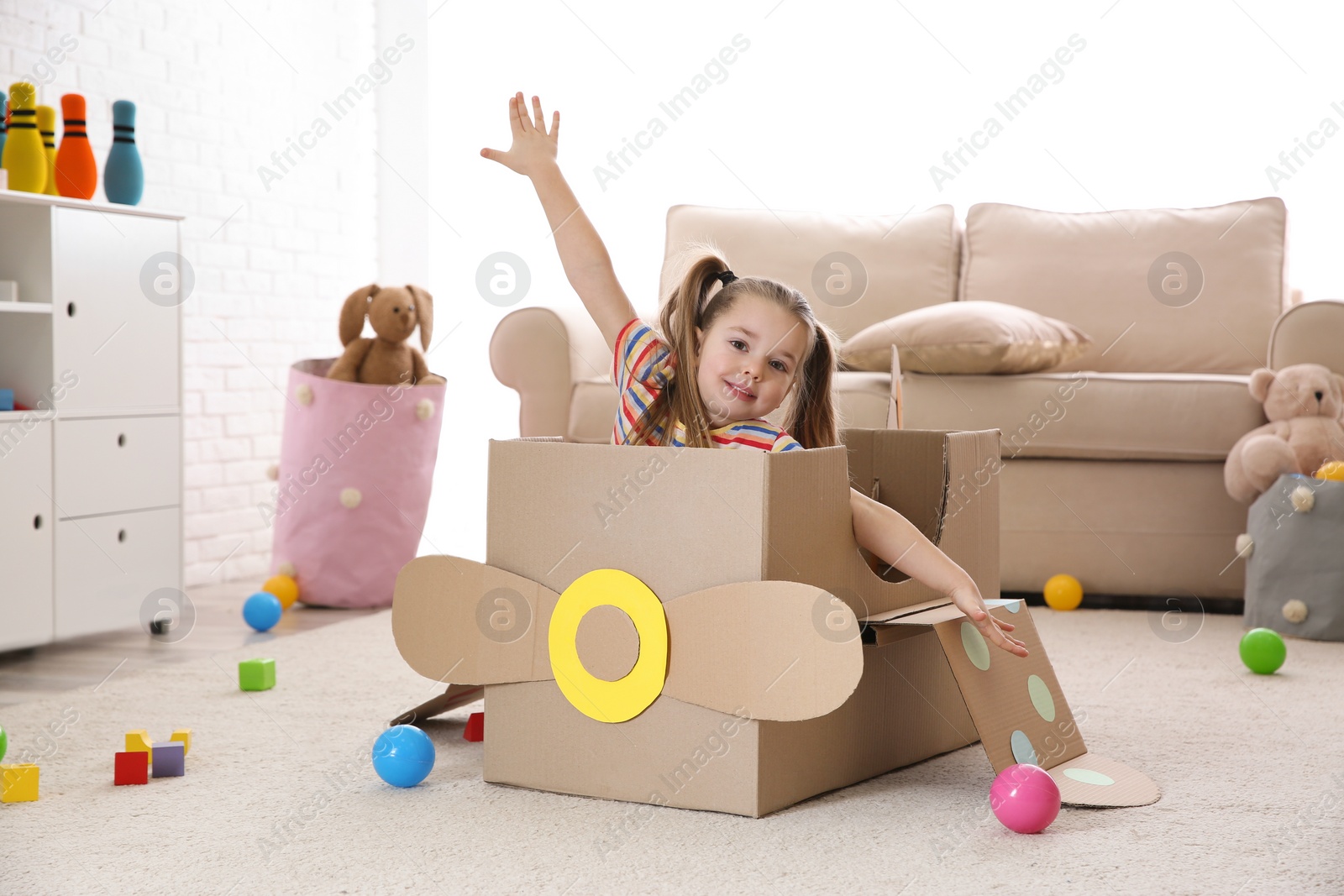 Photo of Cute little child playing with cardboard plane at home