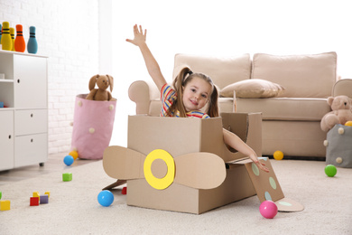 Photo of Cute little child playing with cardboard plane at home