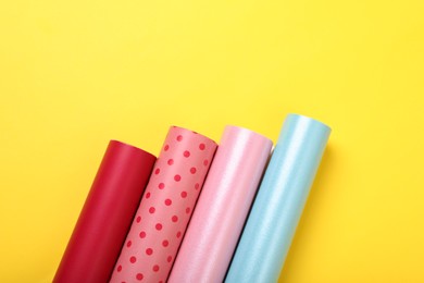 Photo of Rolls of colorful wrapping papers on yellow background, flat lay. Space for text