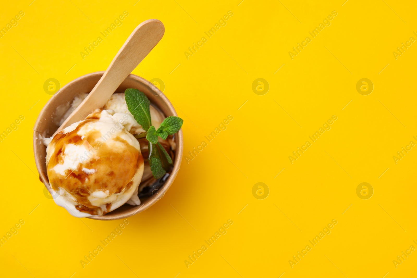 Photo of Scoops of ice cream with caramel sauce and mint leaves on yellow table, top view. Space for text