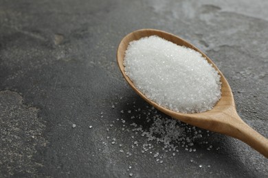 Photo of Spoon with granulated sugar on grey textured table, closeup. Space for text