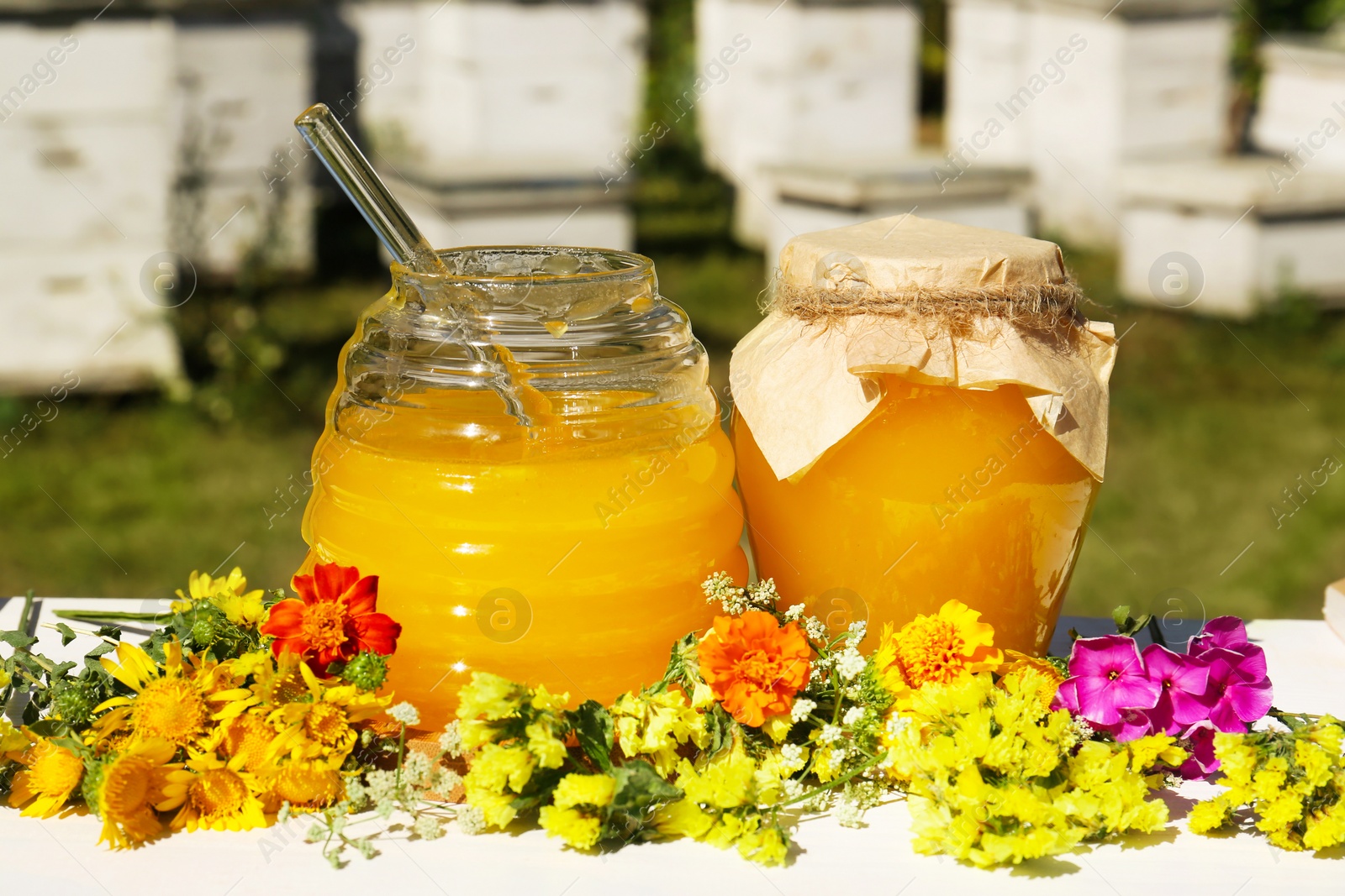 Photo of Delicious fresh honey and beautiful flowers on white wooden table in apiary