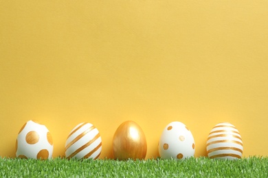 Photo of Line of traditional Easter eggs decorated with golden paint on green lawn against color background, space for text