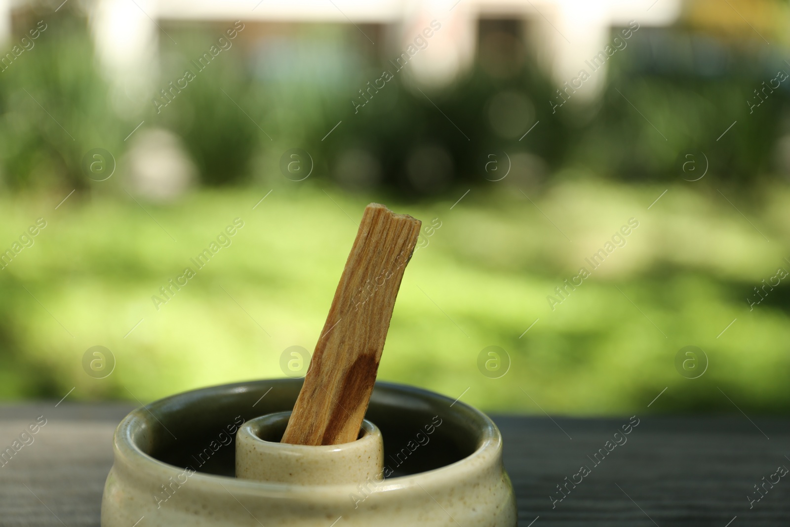 Photo of Palo santo stick in holder on wooden surface outdoors, closeup. Space for text