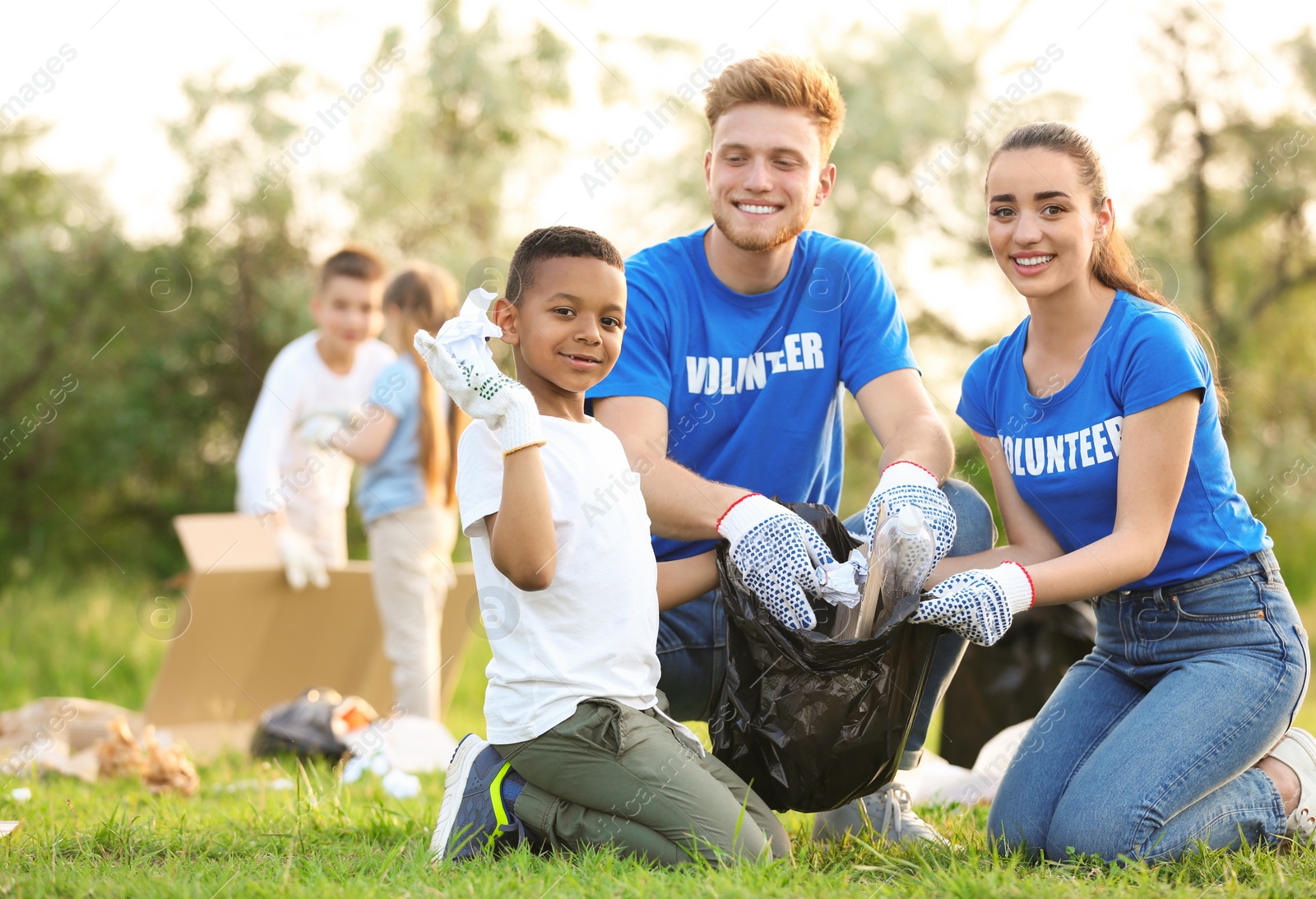 Photo of Little African-American boy collecting trash with volunteers in park