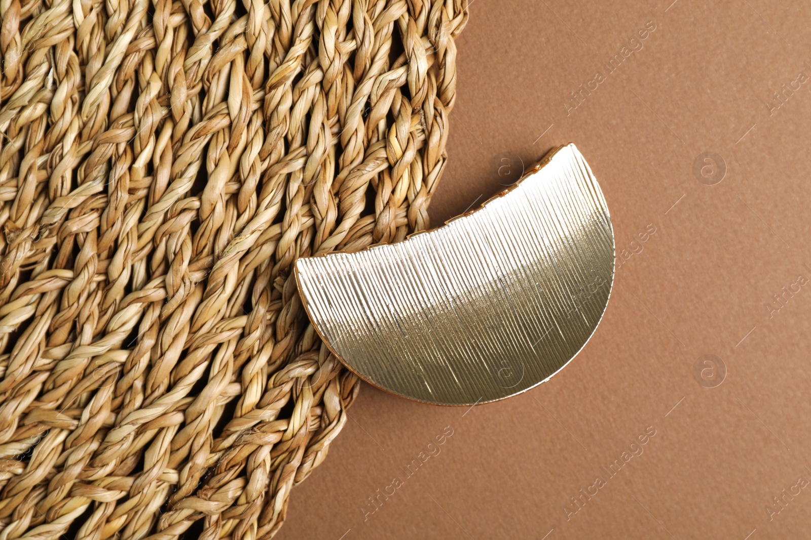 Photo of Stylish hair clip and wicker mat on brown background, top view