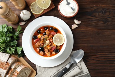 Meat solyanka soup with sausages, olives and vegetables served on wooden table, flat lay. Space for text