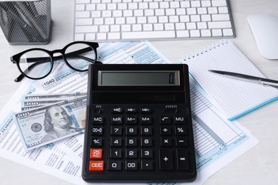 Photo of Tax accounting. Calculator, documents, money, stationery and glasses on light grey table