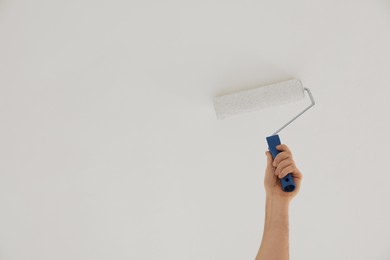 Photo of Worker painting ceiling with roller indoors, closeup. Space for text