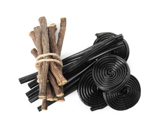 Tasty black candies and dried sticks of liquorice root on white background, top view