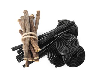 Photo of Tasty black candies and dried sticks of liquorice root on white background, top view