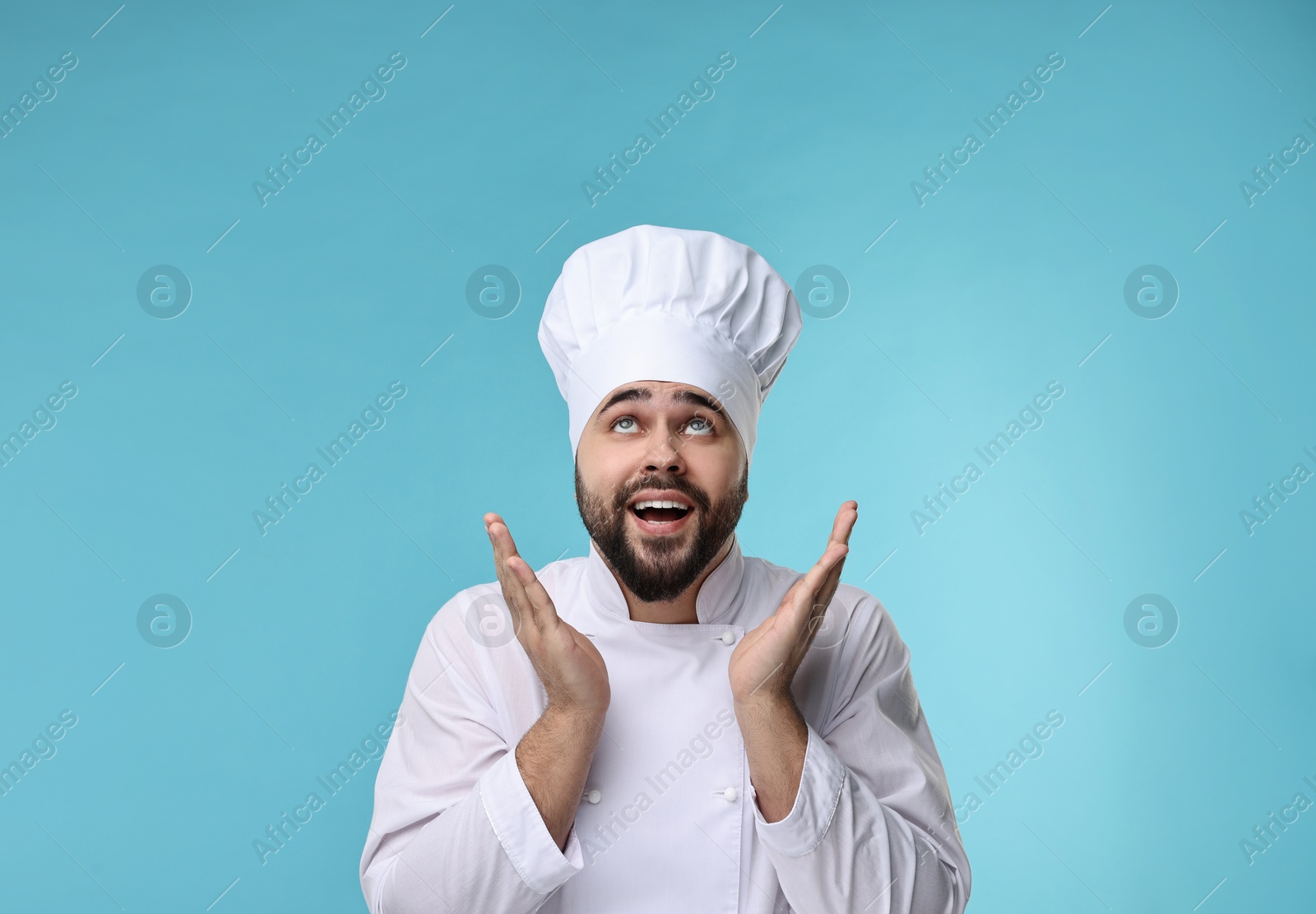 Photo of Happy young chef in uniform on light blue background