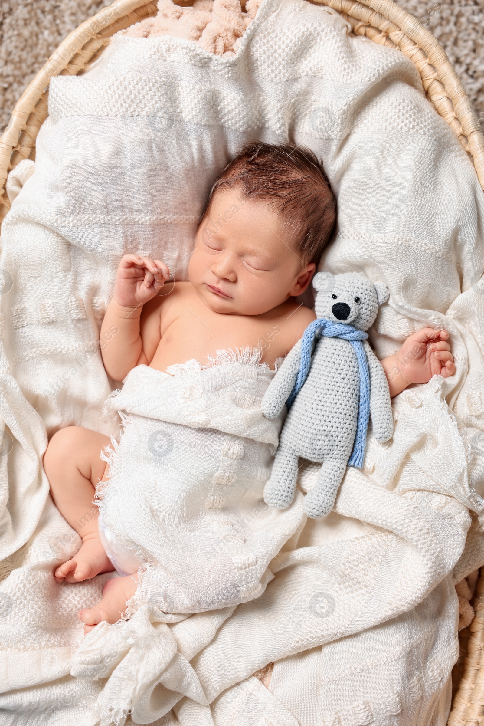 Photo of Cute newborn baby sleeping with toy bear on white blanket in wicker crib, top view