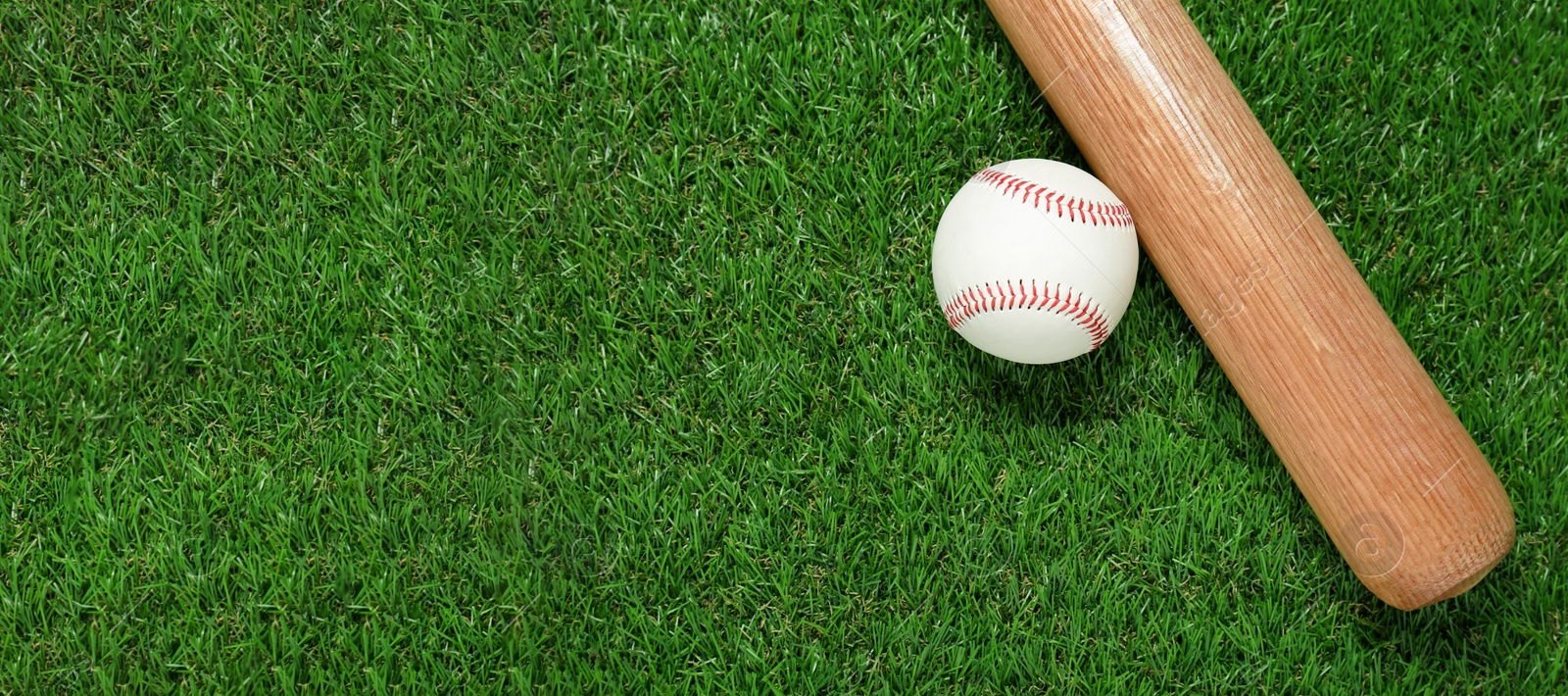 Photo of Wooden baseball bat and ball on green grass, flat lay. Sports equipment