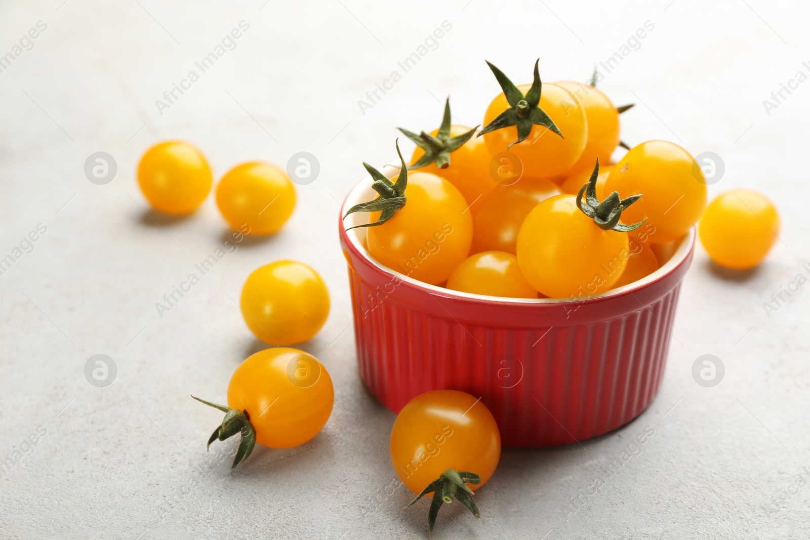 Photo of Ripe yellow tomatoes in bowl on grey table