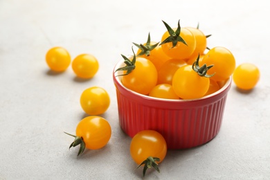 Photo of Ripe yellow tomatoes in bowl on grey table